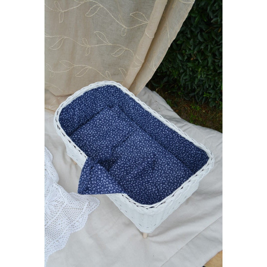 Leagă pentru păpuși din ratan, de culoare albă, cu o pătură albastră.