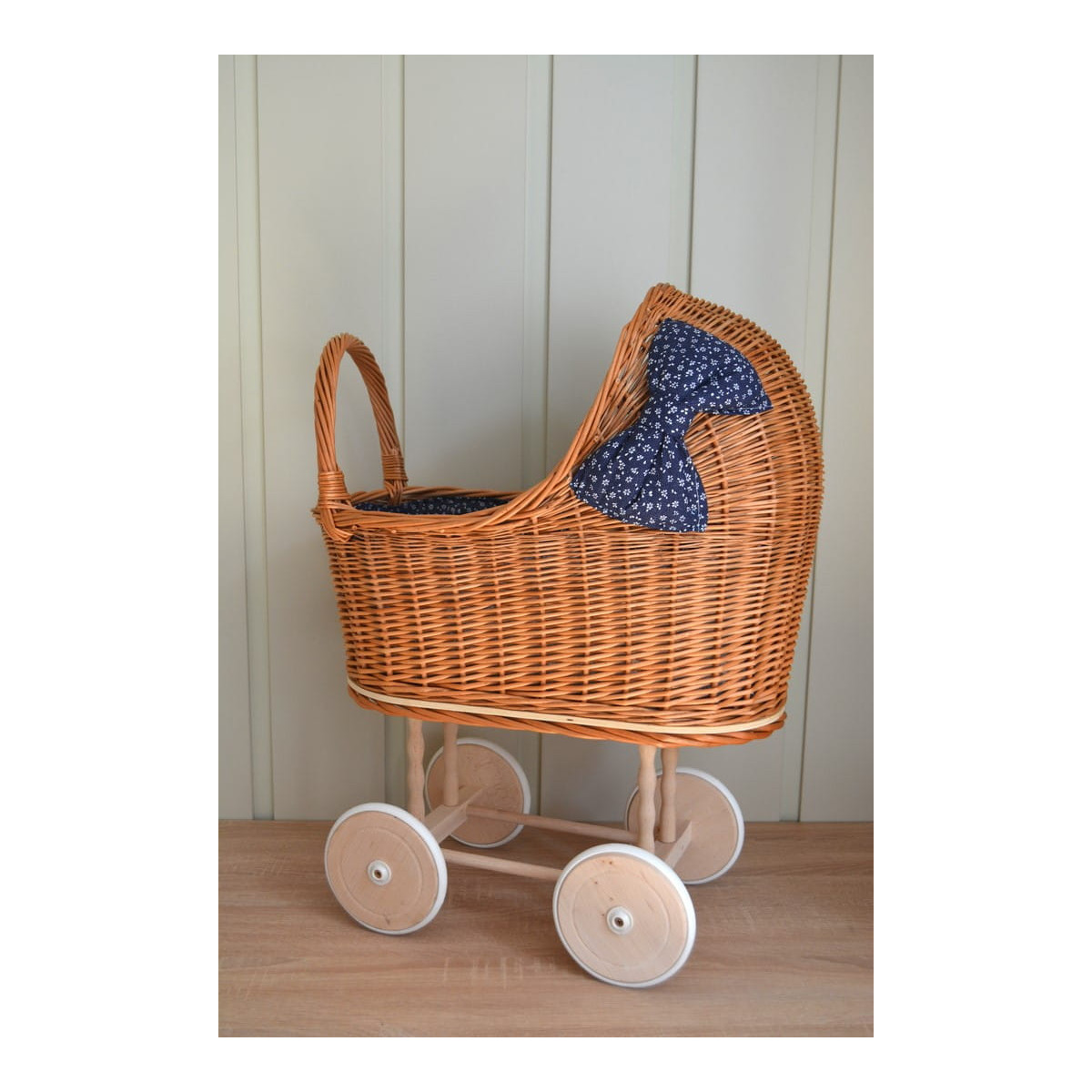 Cărucior din rattan pentru copii, cu fundiță albastră și roți din cauciuc.