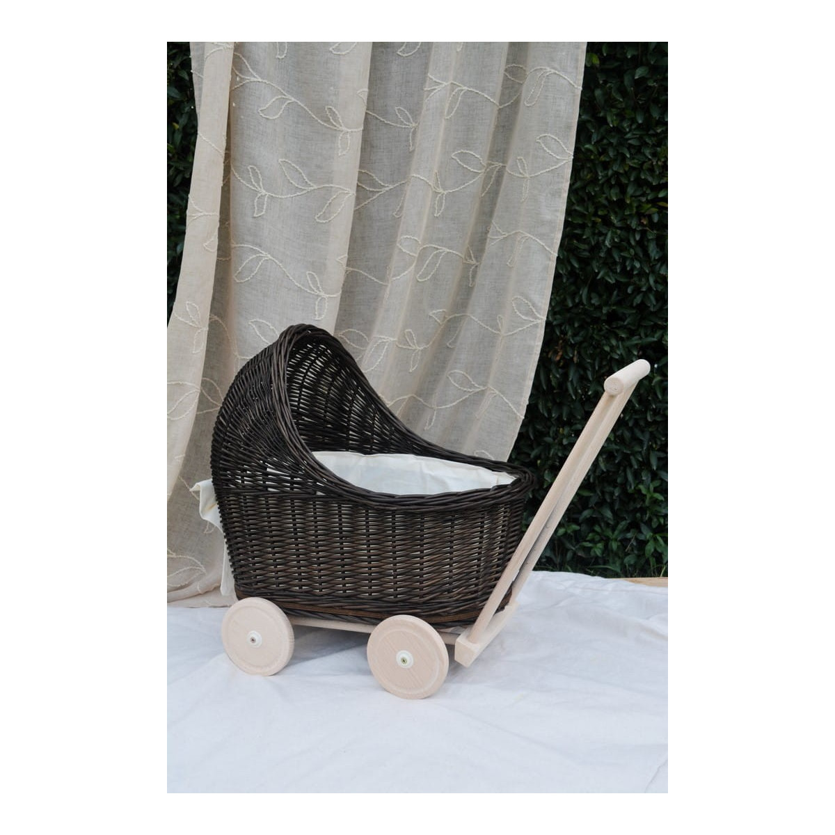 Cărucior pentru copii din rattan original, de culoare brownă, cu o fundiță albă.