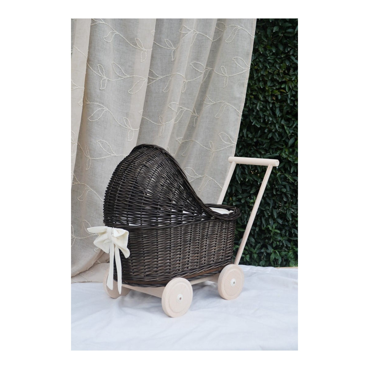 Cărucior pentru copii din rattan original, de culoare brownă, cu o fundiță albă.