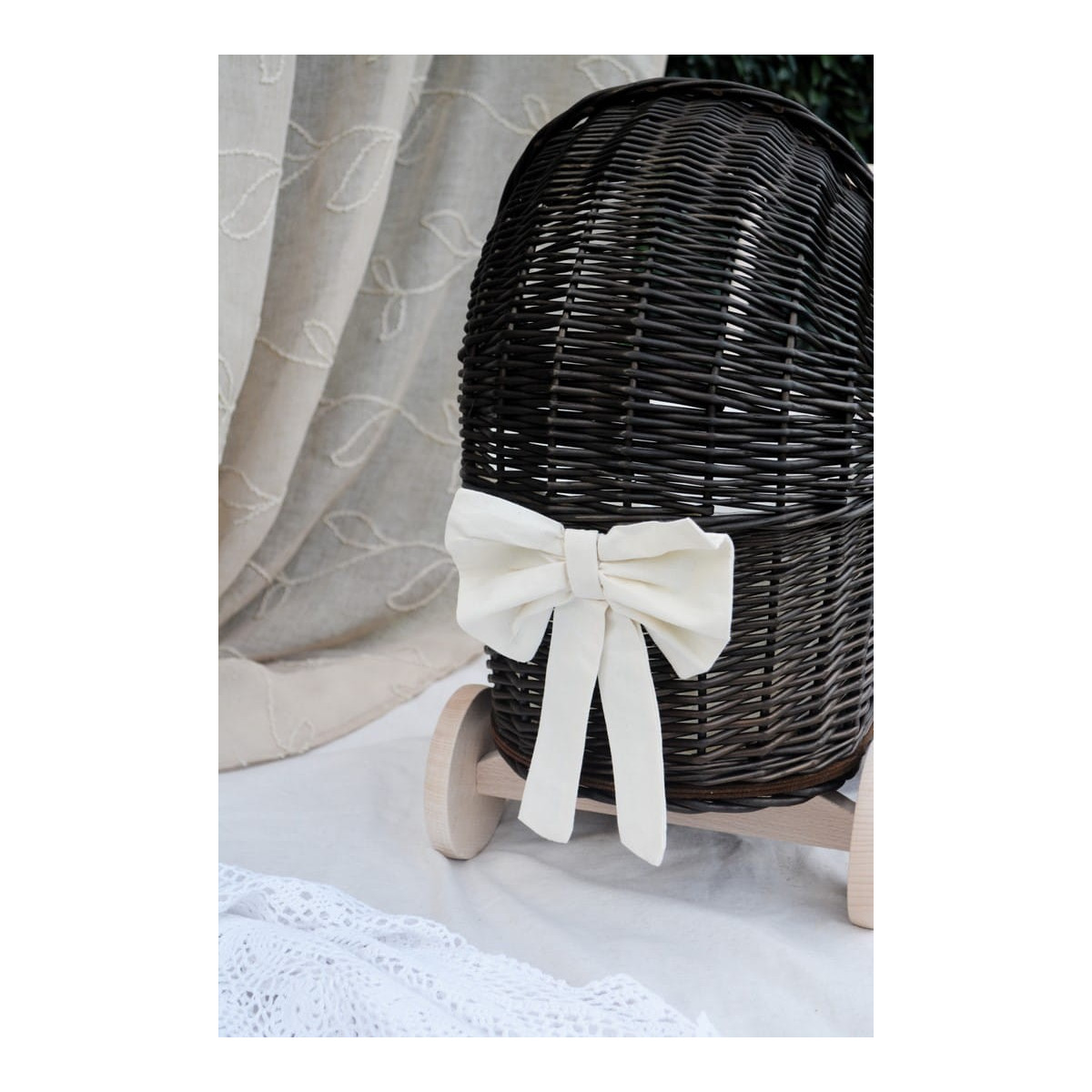 Cărucior pentru copii din rattan original, de culoare brownă, cu o fundiță albă.