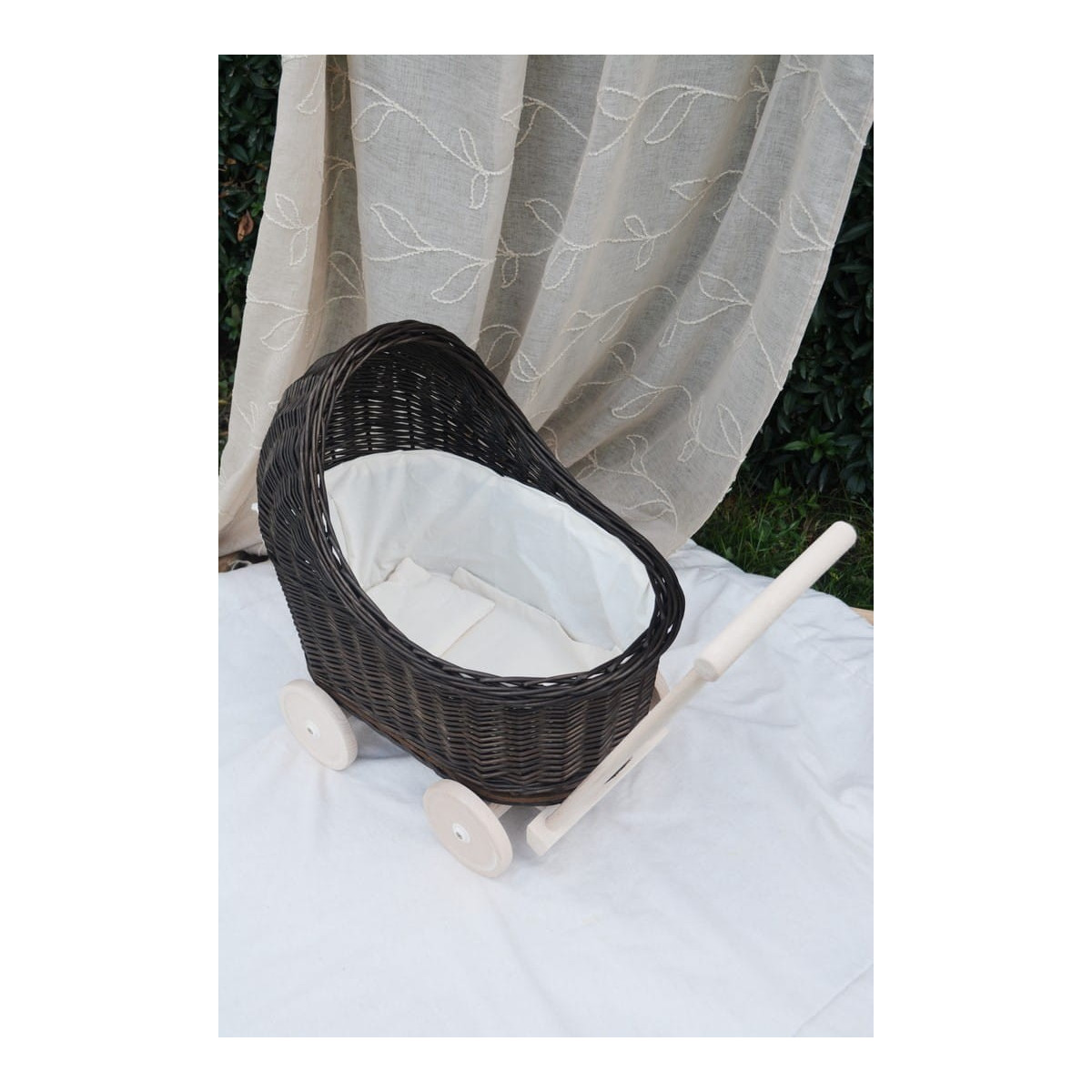 Cărucior pentru copii din rattan original, de culoare brownă, cu o fundiță albă.